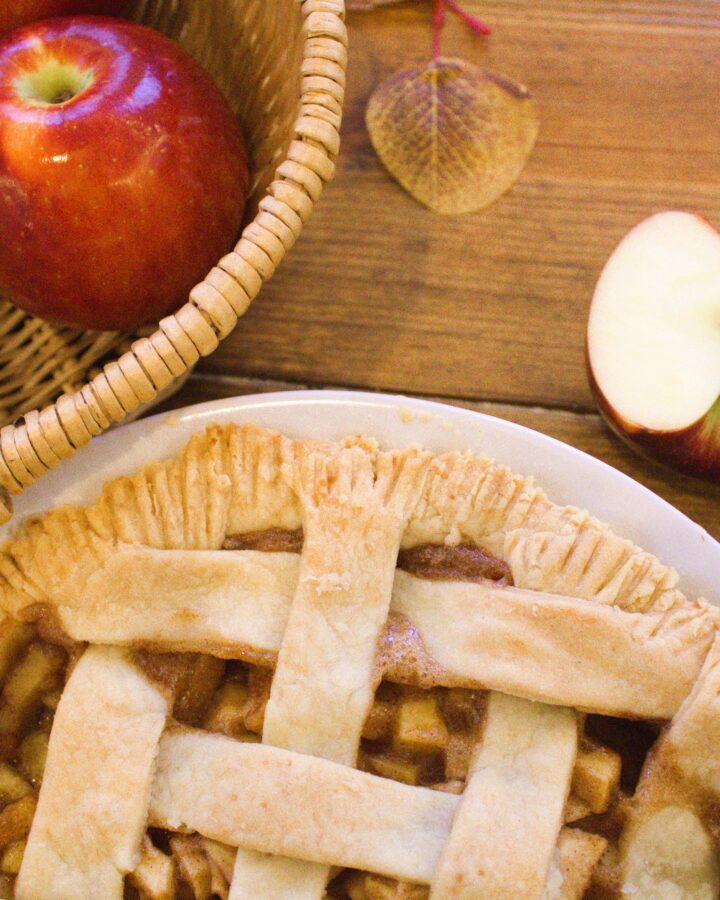 A wooden table displaying a basket of apples and an apple pie