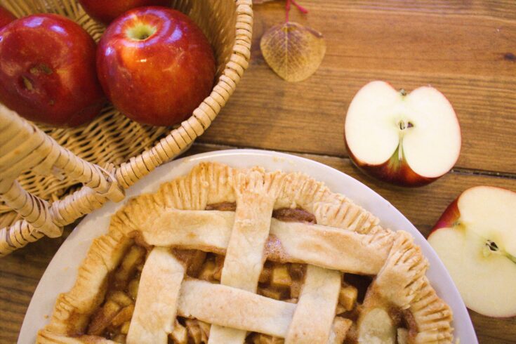 A wooden table displaying a basket of apples and an apple pie