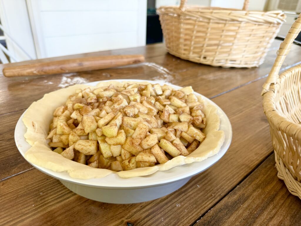 A wood table with woven baskets, and an apple pie that is still raw