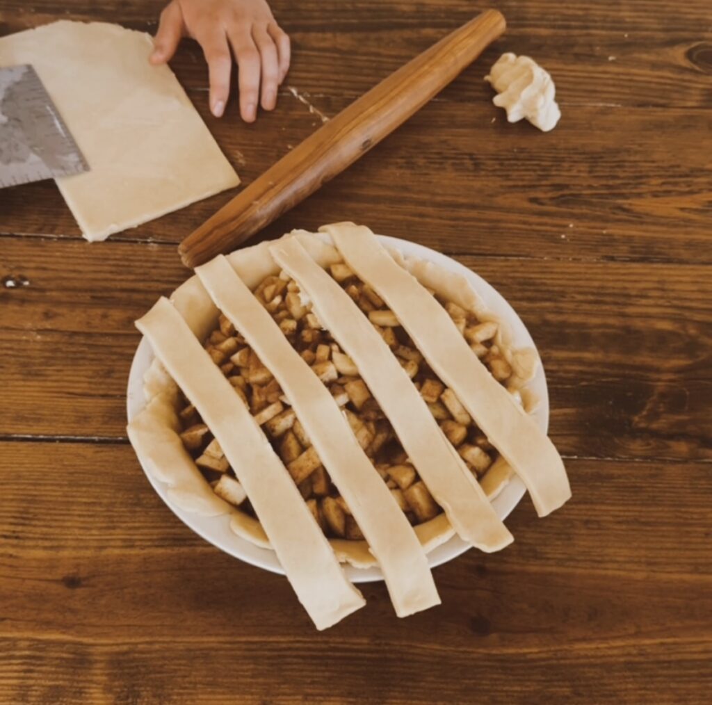 A wooden table with a rolling pin and a half made apple pie