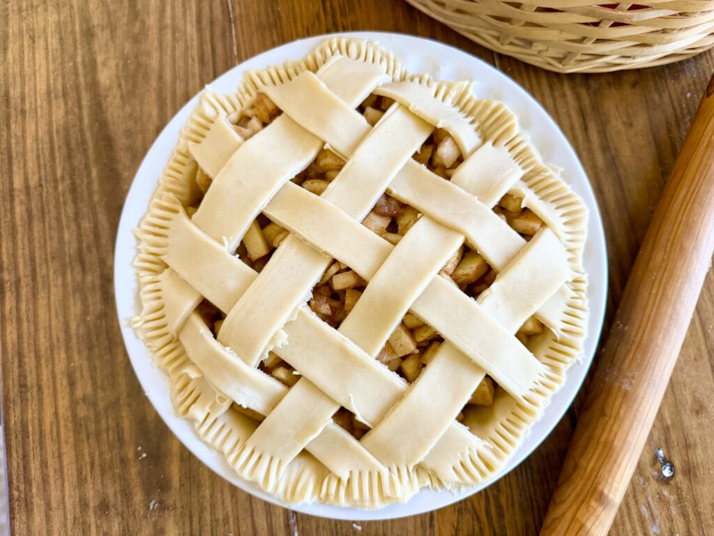 A wooden table holding an raw apple pie with a rolling pin next to it