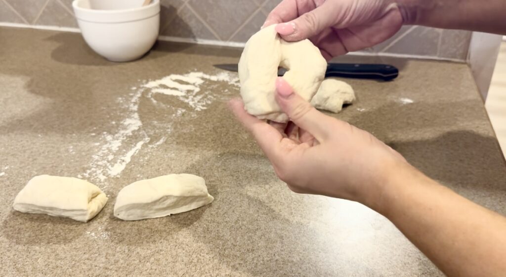 Hand demonstrating how to shape sourdough bagels.