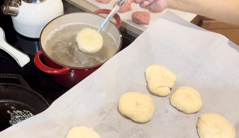 A pot of boiling water next to a baking sheet of sourdough bagels.