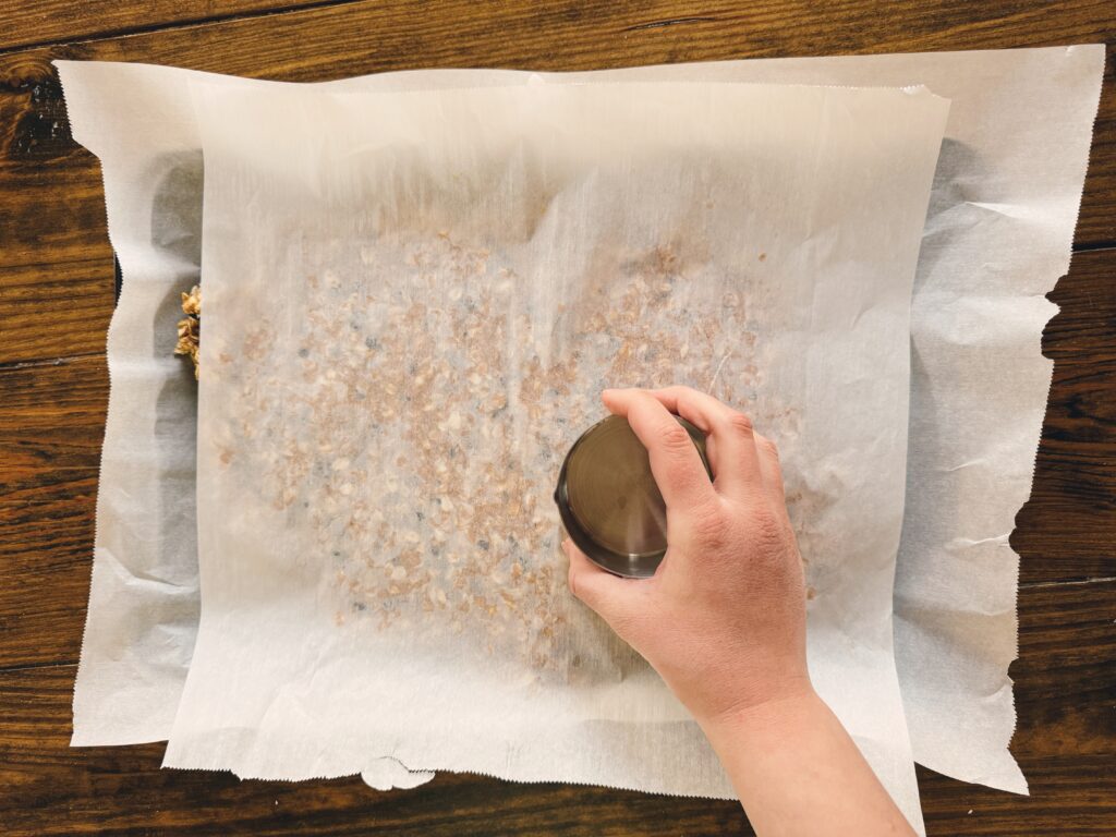 A girl using a cup to press down a mixture covered with parchment paper.