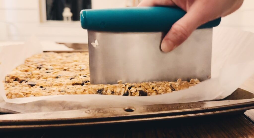 A girl using a bench scraper to cut granola.