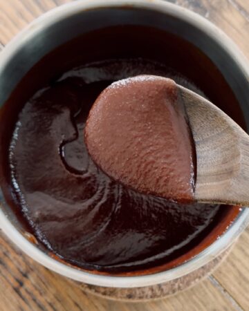 A wooden table holding a saucepan with barbeque sauce.