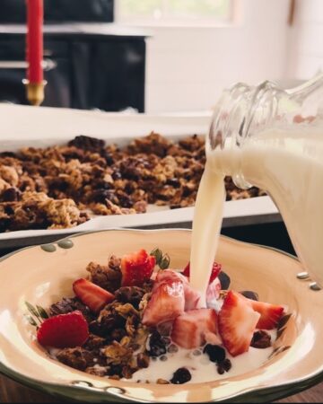 A table holding a baking sheet of granola and milk splashing into a bowl of granola.