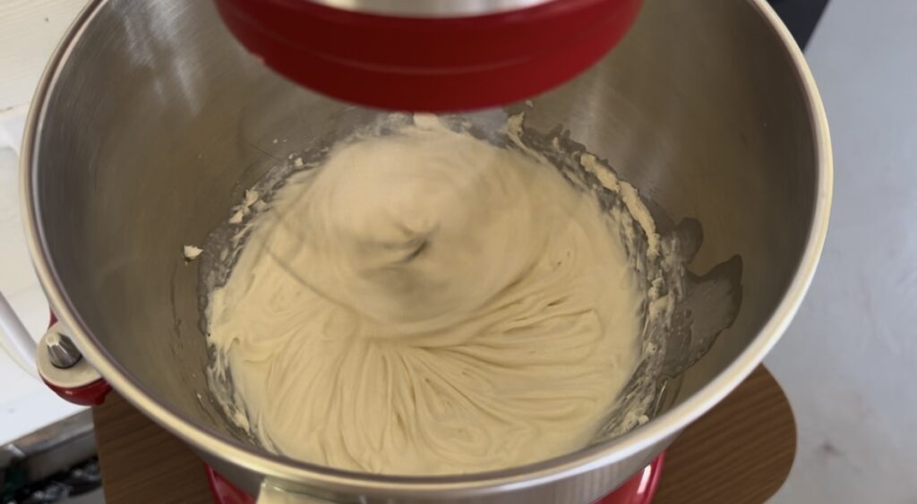 A stand mixer with cream cheese and sugar inside being mixed.