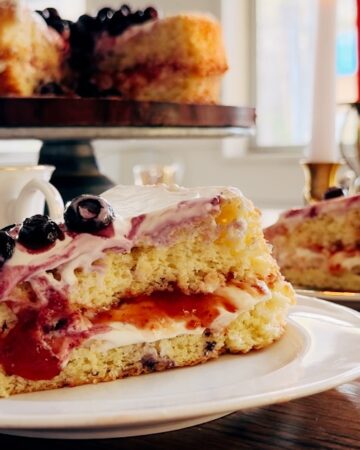 A close up of a sponge cake on a plate with frosting and blueberries.