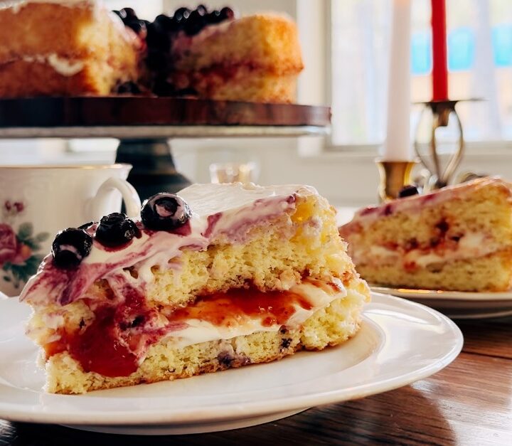 A close up of a sponge cake on a plate with frosting and blueberries.
