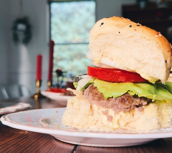 A white plate holding a homemade hamburger with fresh vegetables.