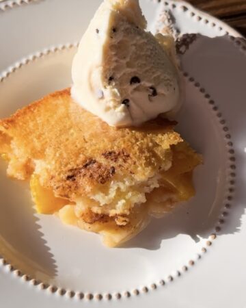 A white plate holding homemade peach cobbler topped with ice cream.